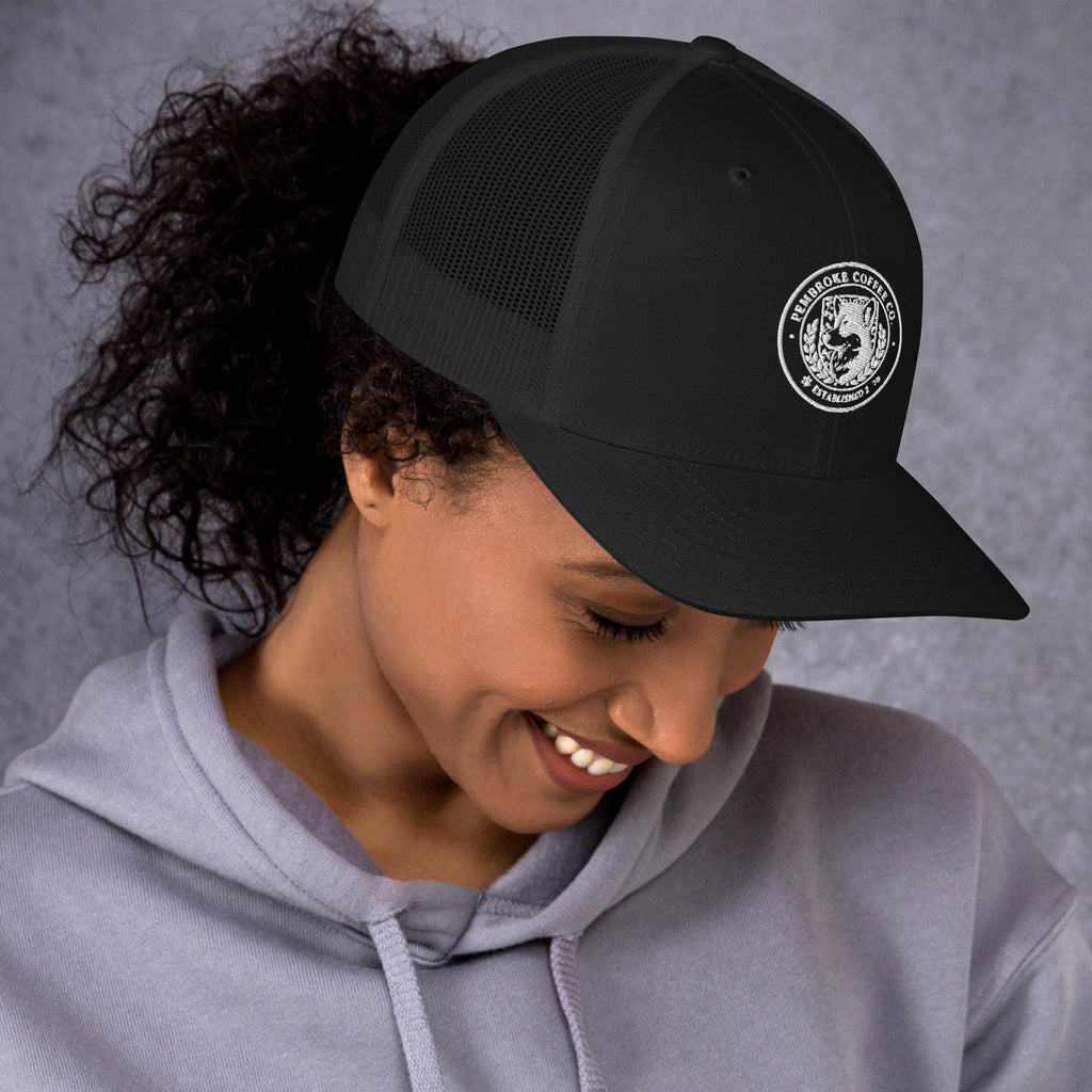 Trucker Cap in black worn by a smiling woman with curly hair, showcasing the stylish mesh back and logo.