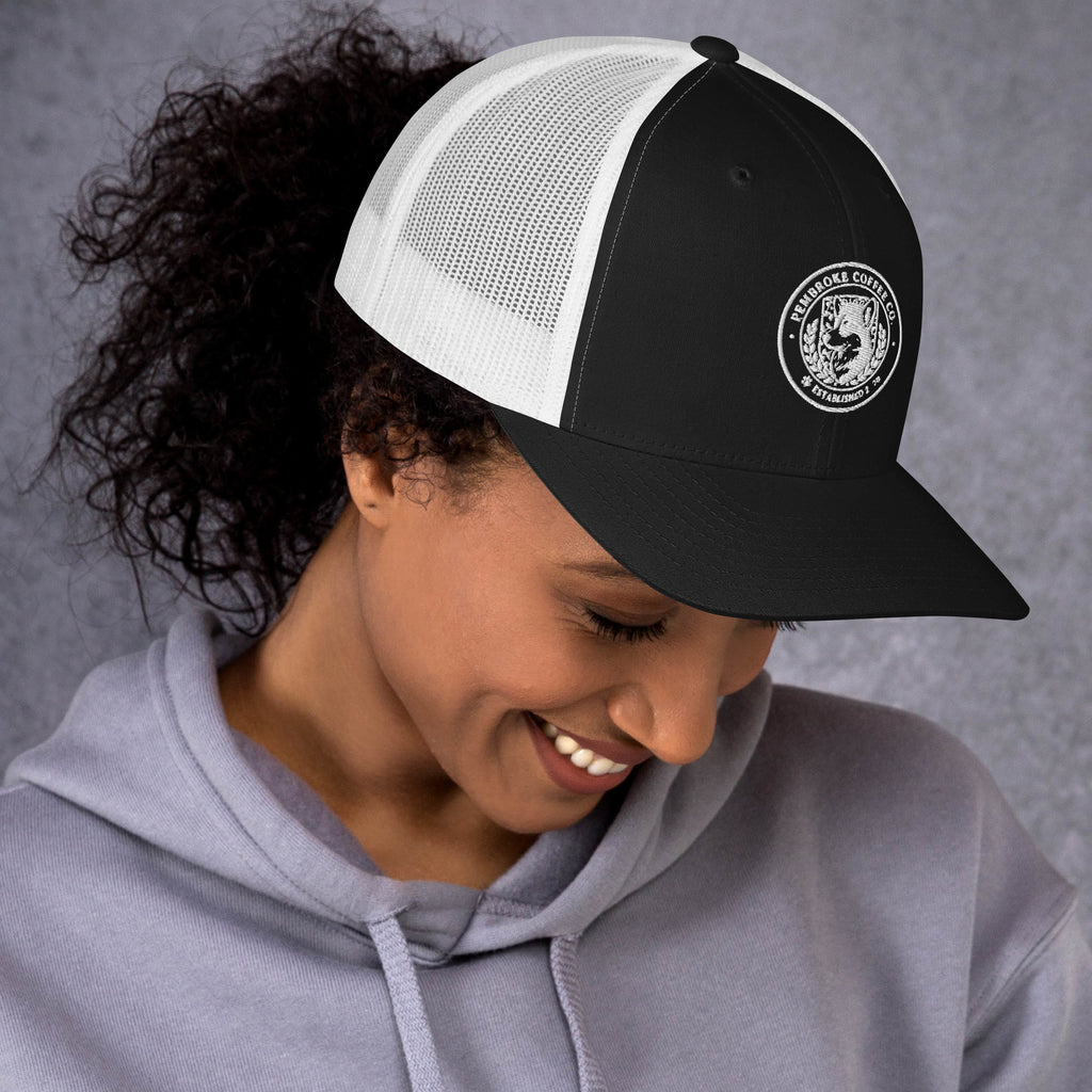 Trucker Cap with a black front, white mesh back, worn by a smiling woman in a gray hoodie.