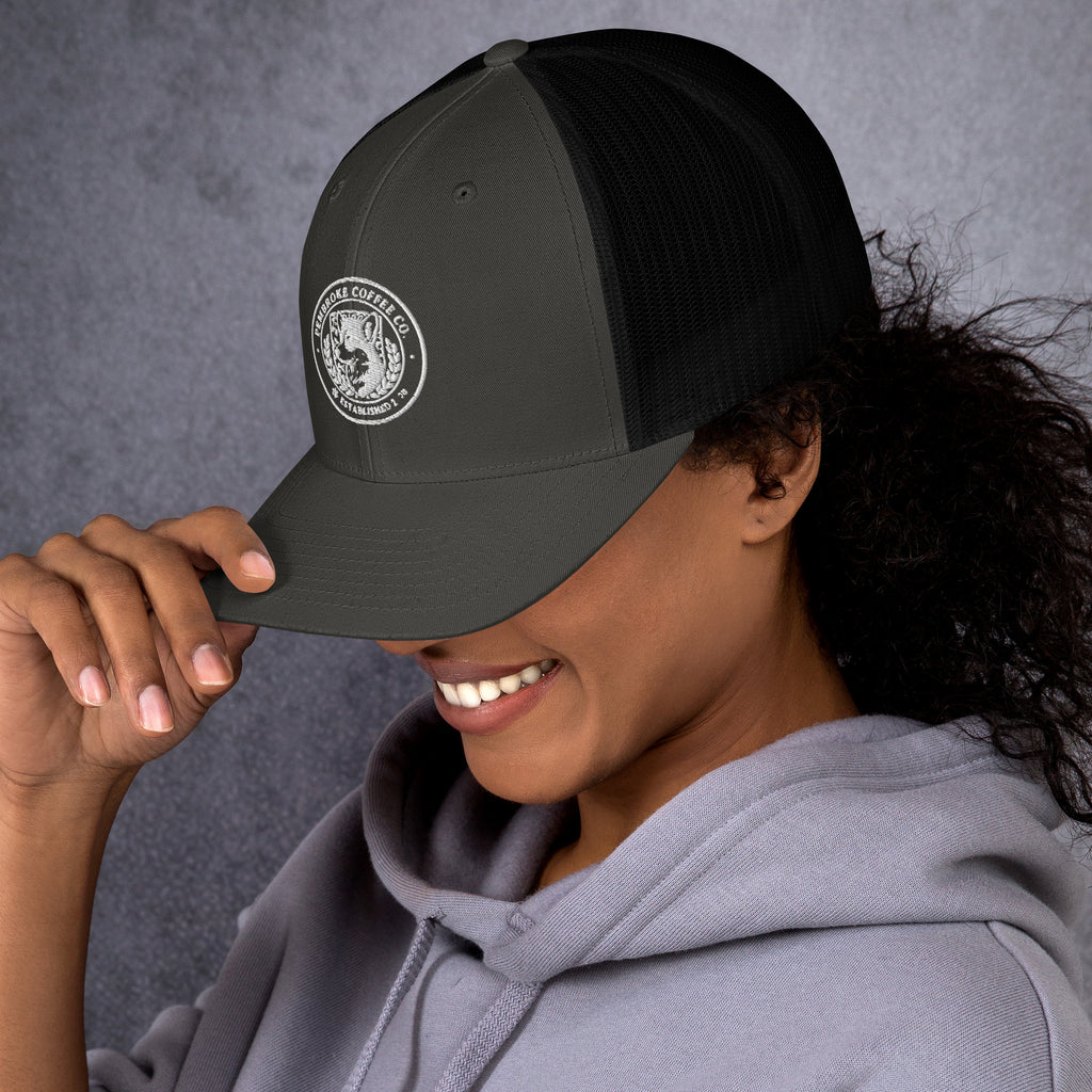 Smiling person wearing a Trucker Cap with a logo, showcasing the structured six-panel design and mesh back.