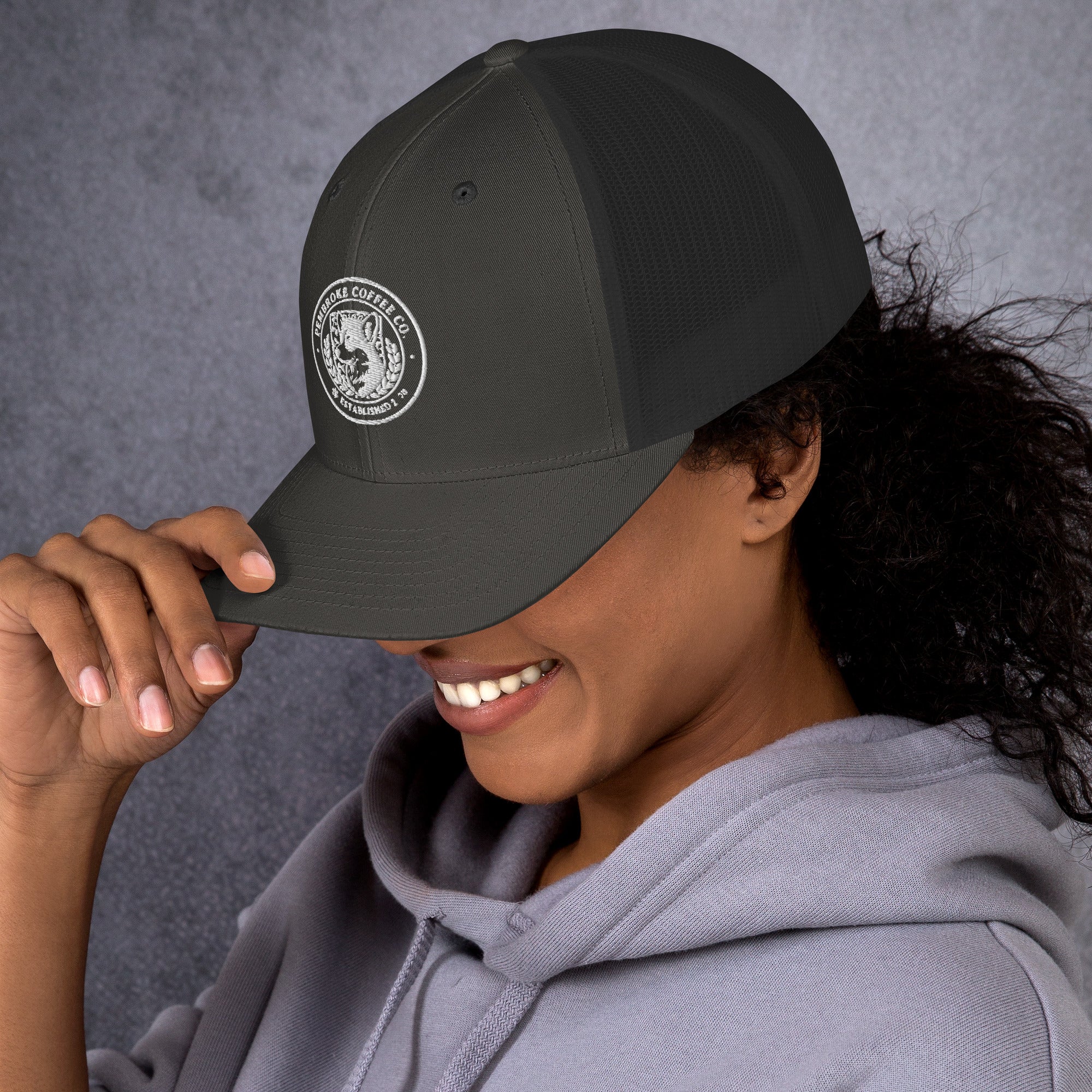 Woman wearing a dark trucker cap with a logo, showcasing a stylish look and comfortable design.
