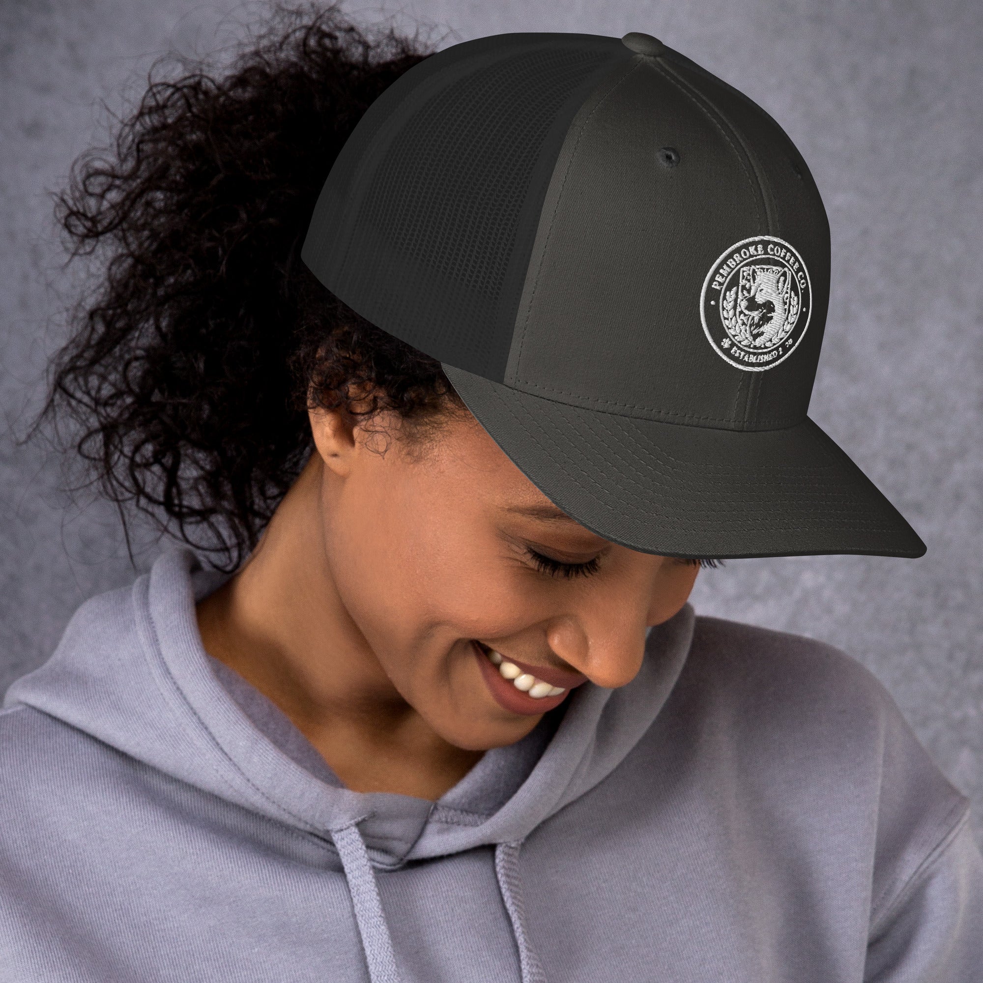 Woman wearing a Trucker Cap with a logo, smiling while showcasing the cap's stylish design.