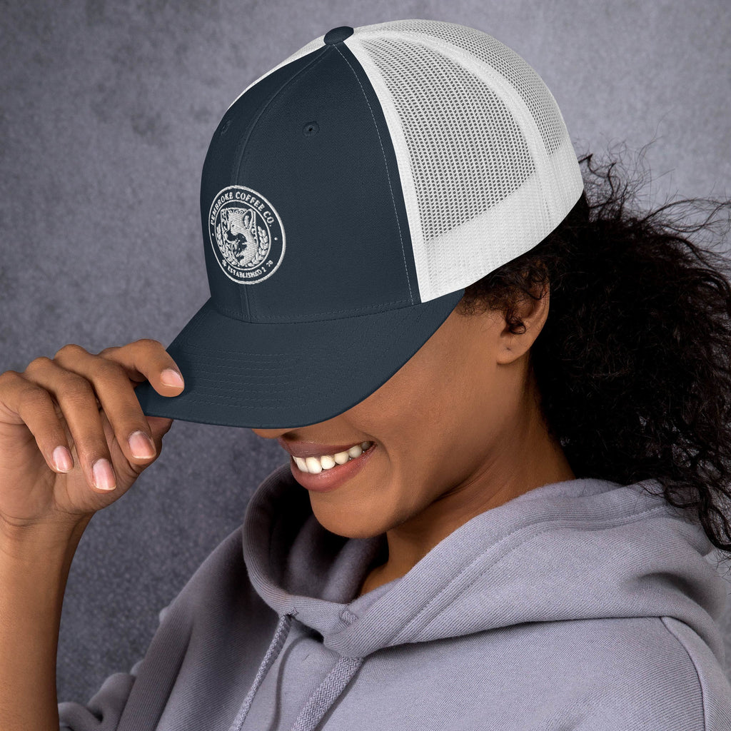 Woman wearing a dark grey trucker cap with mesh back, smiling and looking down, perfect for sunny days.