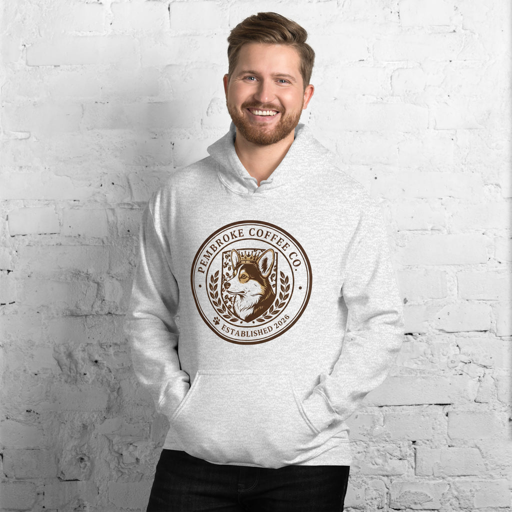 A man wearing a Unisex Hoodie featuring Pembroke Coffee Co logo against a brick wall background.