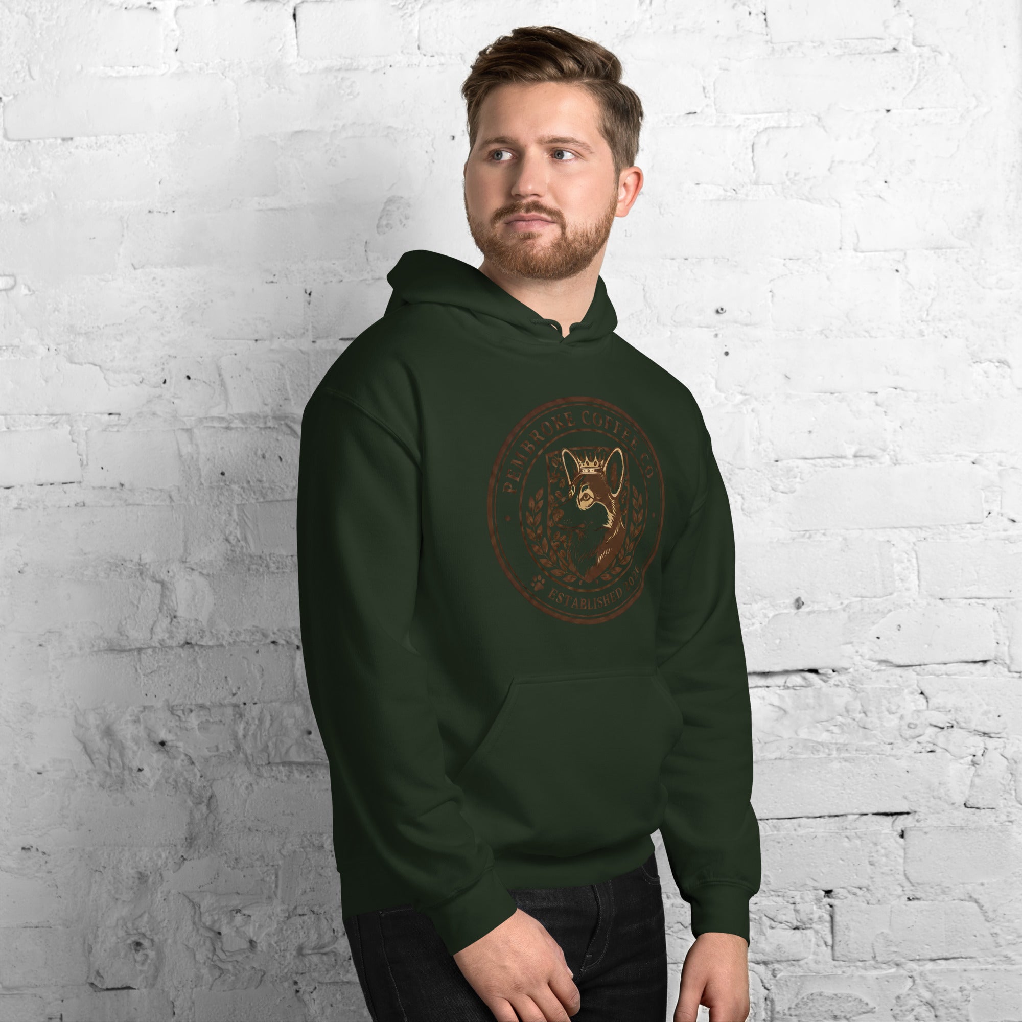 Unisex Hoodie in dark green worn by a man against a white brick wall, showcasing a stylish and cozy design.