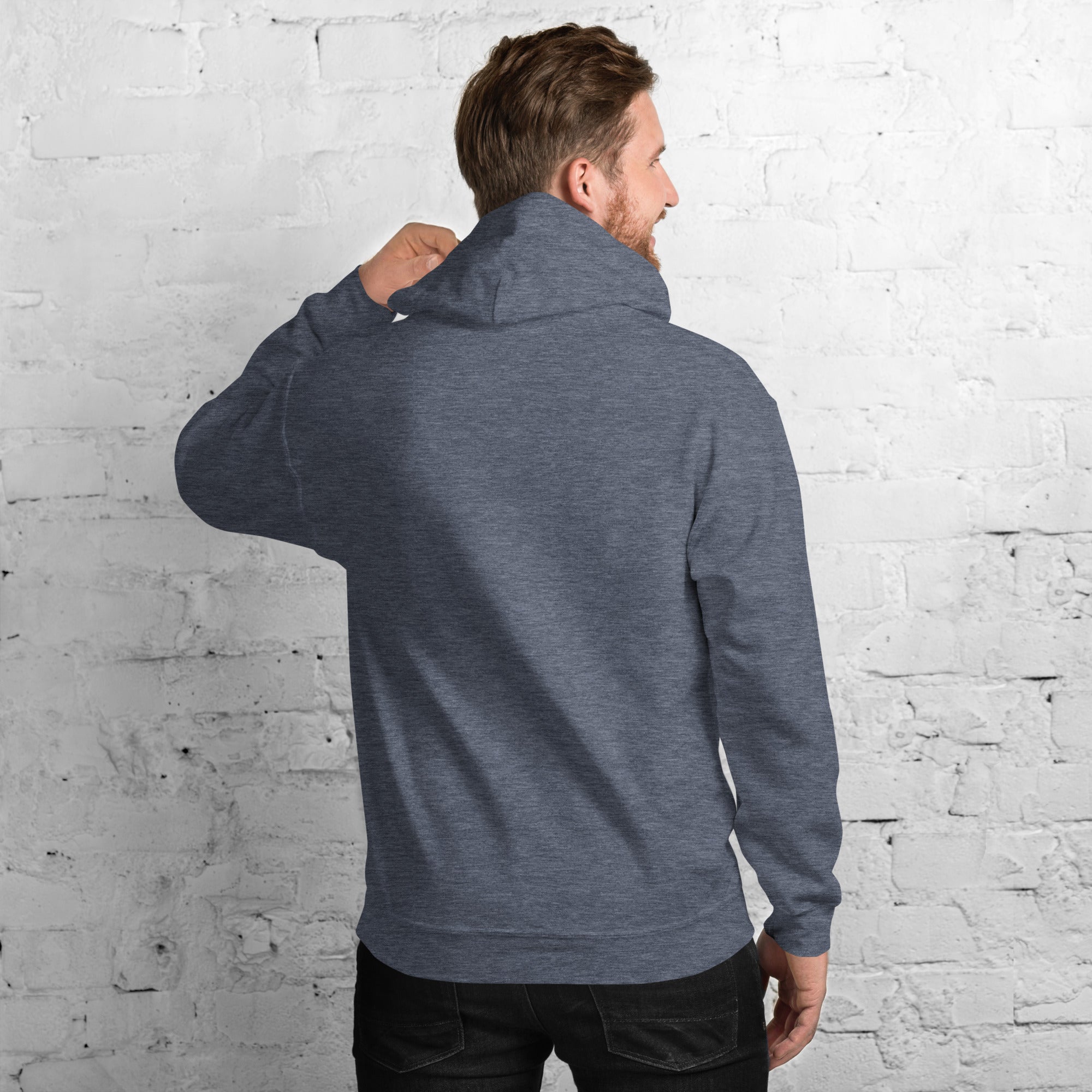 Back view of a man wearing a cozy Unisex Hoodie against a brick wall.