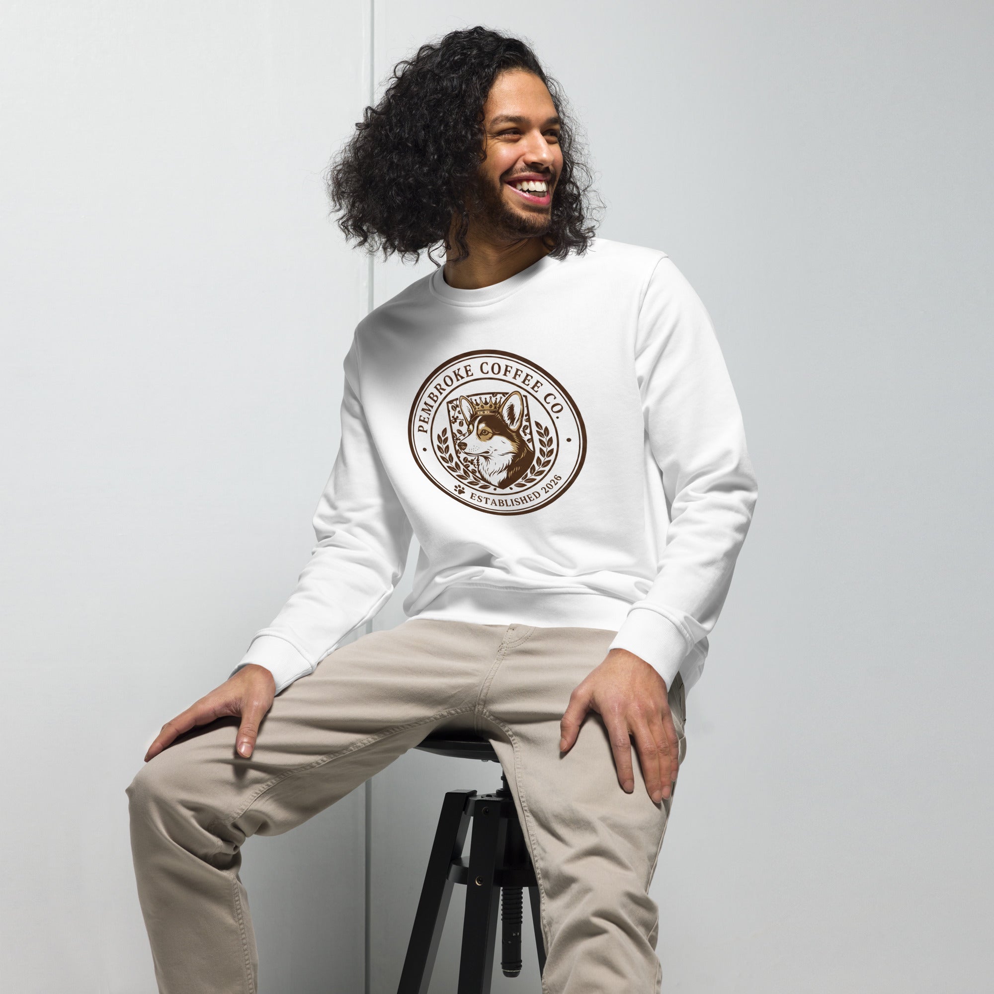 Unisex organic sweatshirt featuring a coffee logo, modeled by a man with curly hair, sitting casually.